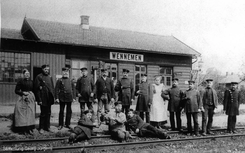 Das erste Bahnhofsgebäude von Wennemen um 1873. Der Zugverkehr scheint noch selten zu sein, sonst hätte man sich nicht zum Umtrunk und Foto im Gleis versammeln können